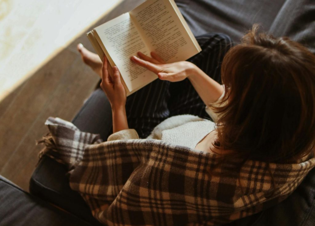 Woman relaxing with a book on a cozy sofa bathed in sunlight.