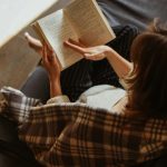Woman relaxing with a book on a cozy sofa bathed in sunlight.