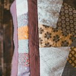 Close-up of a patchwork quilt with floral and geometric patterns in earthy tones.